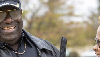 A blind veteran holding his white cane smiles with a friend.