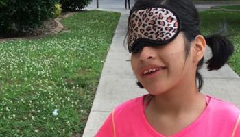 An NFB BELL participant wearing sleepshades smiles while outside.